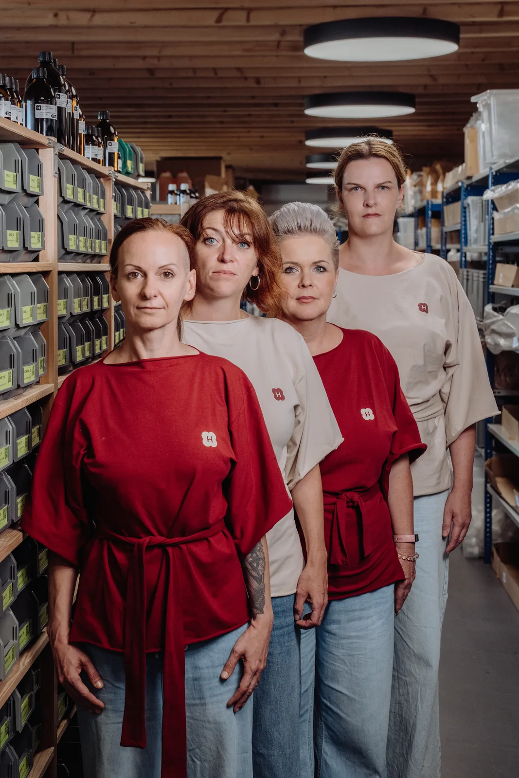 Čtyři lidé z týmu Handymade stojí za sebou v uličce skladu mezi regály se surovinami